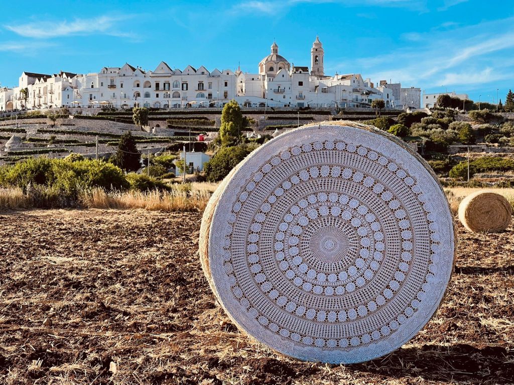 Grande rosone in pietra posato in un campo roccioso, con Ostuni bianca sullo sfondo